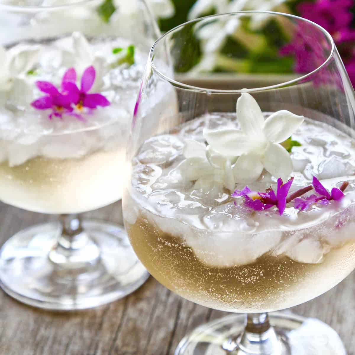 Two glasses filled with St Germain cocktails garnished with tiny purple orchids and white jasmine flowers.