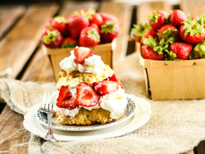 A small plate with strawberry shortcake and a fork with two wood strawberry baskets.