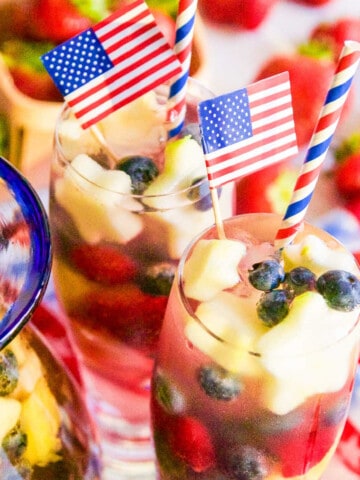 Two tall glasses of white sangria loaded with blueberries, raspberries, strawberries, and apple star garnish.