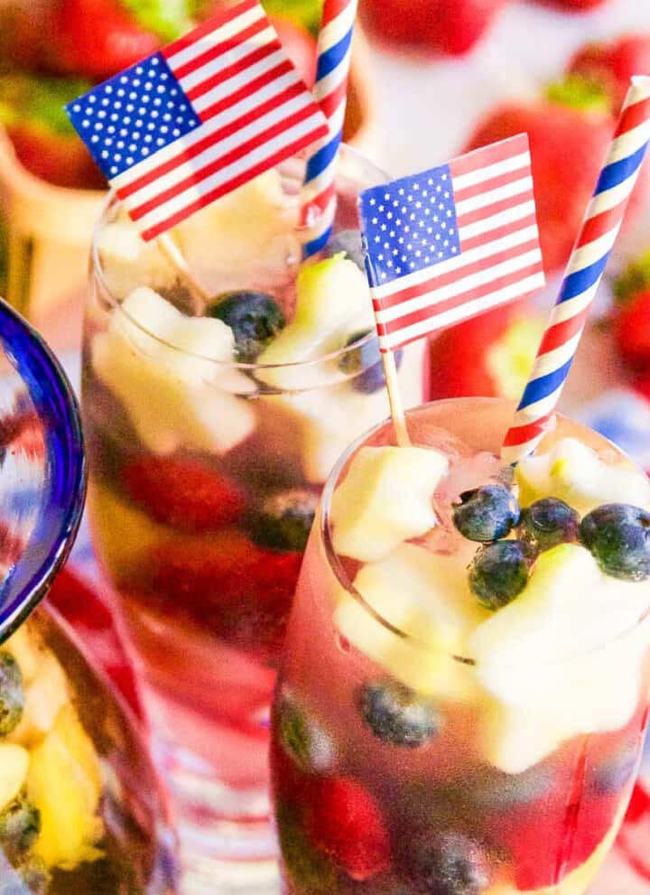 Two tall glasses of white sangria loaded with blueberries, raspberries, strawberries, and apple star garnish.