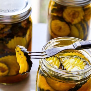 A glass quart jar filled with zucchini pickles with a fork resting on jar spearing a pickle.