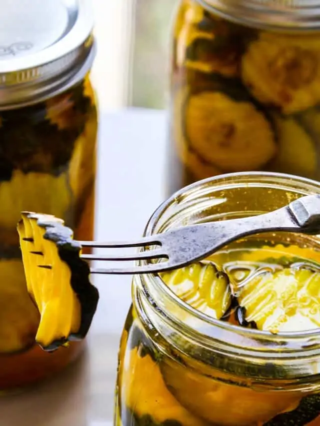 A glass quart jar filled with zucchini pickles with a fork resting on jar spearing a pickle.