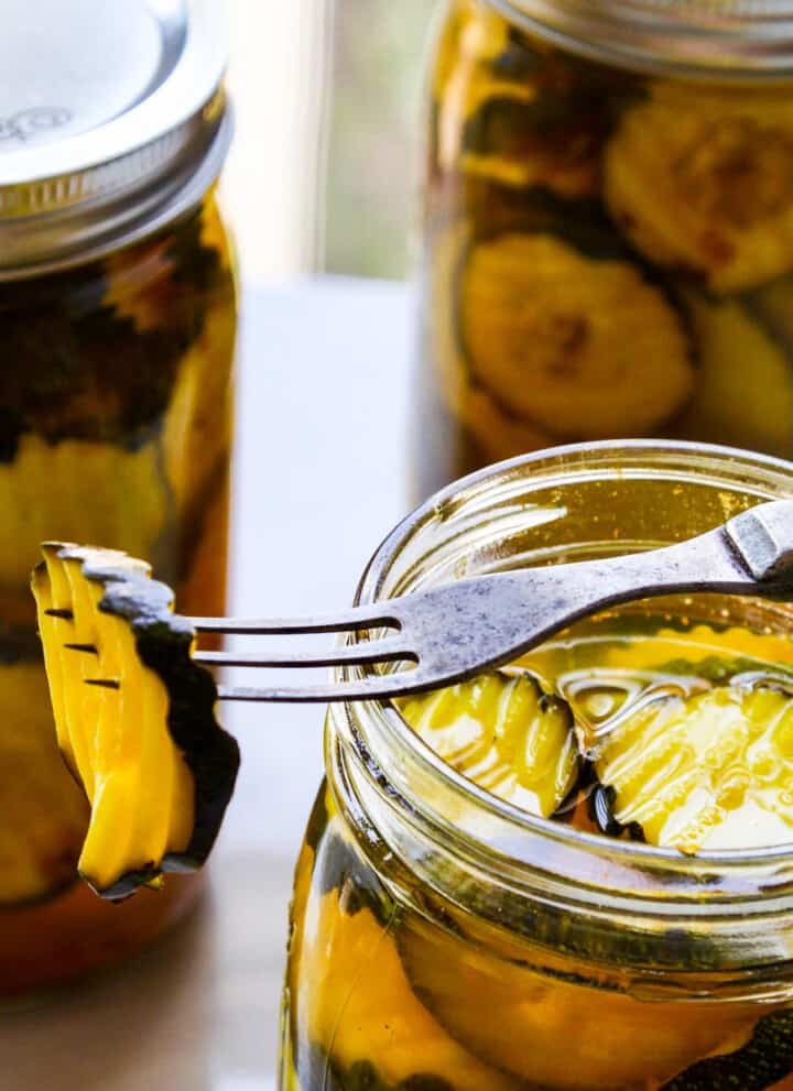 A glass quart jar filled with zucchini pickles with a fork resting on jar spearing a pickle.
