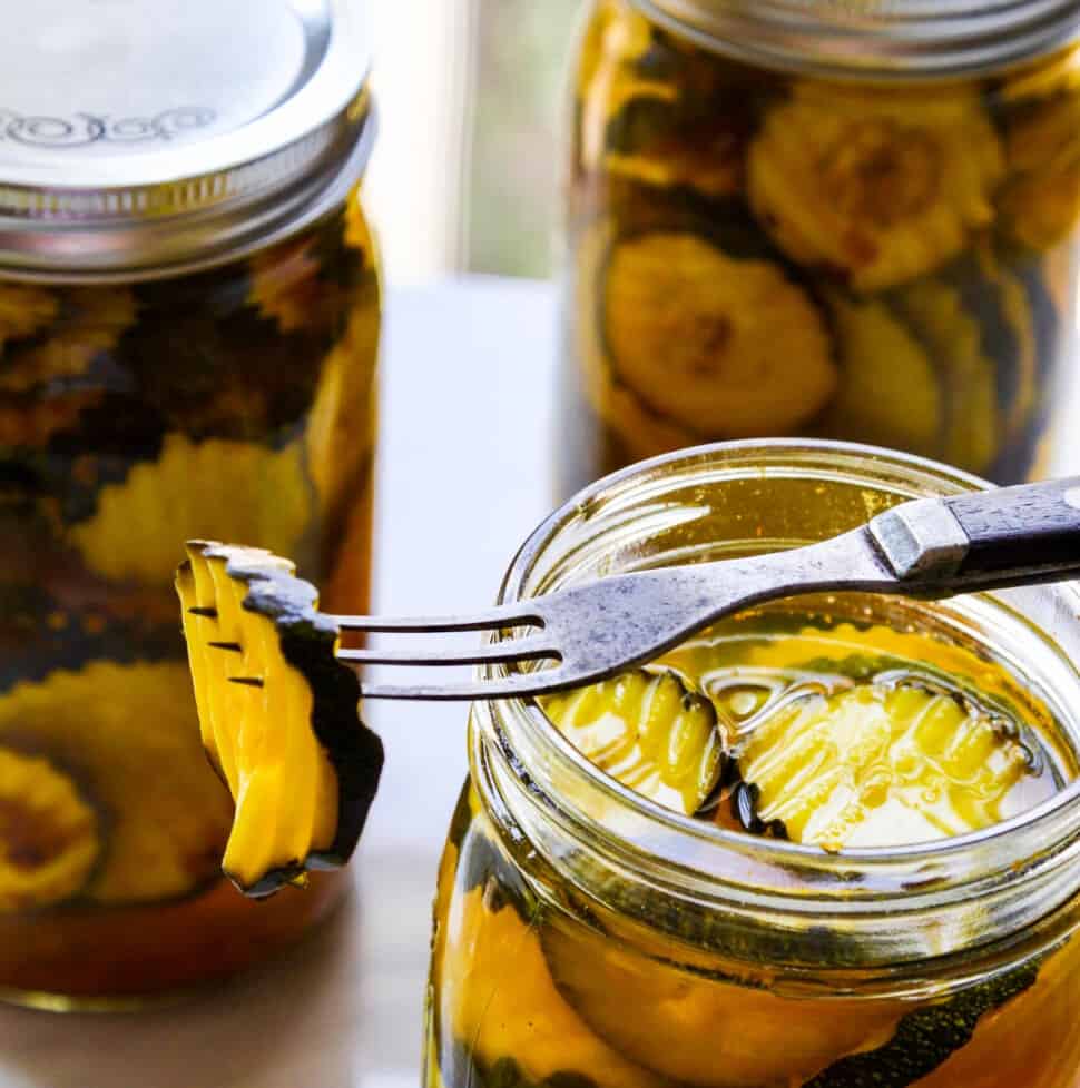 A glass quart jar filled with zucchini pickles with a fork resting on jar spearing a pickle.