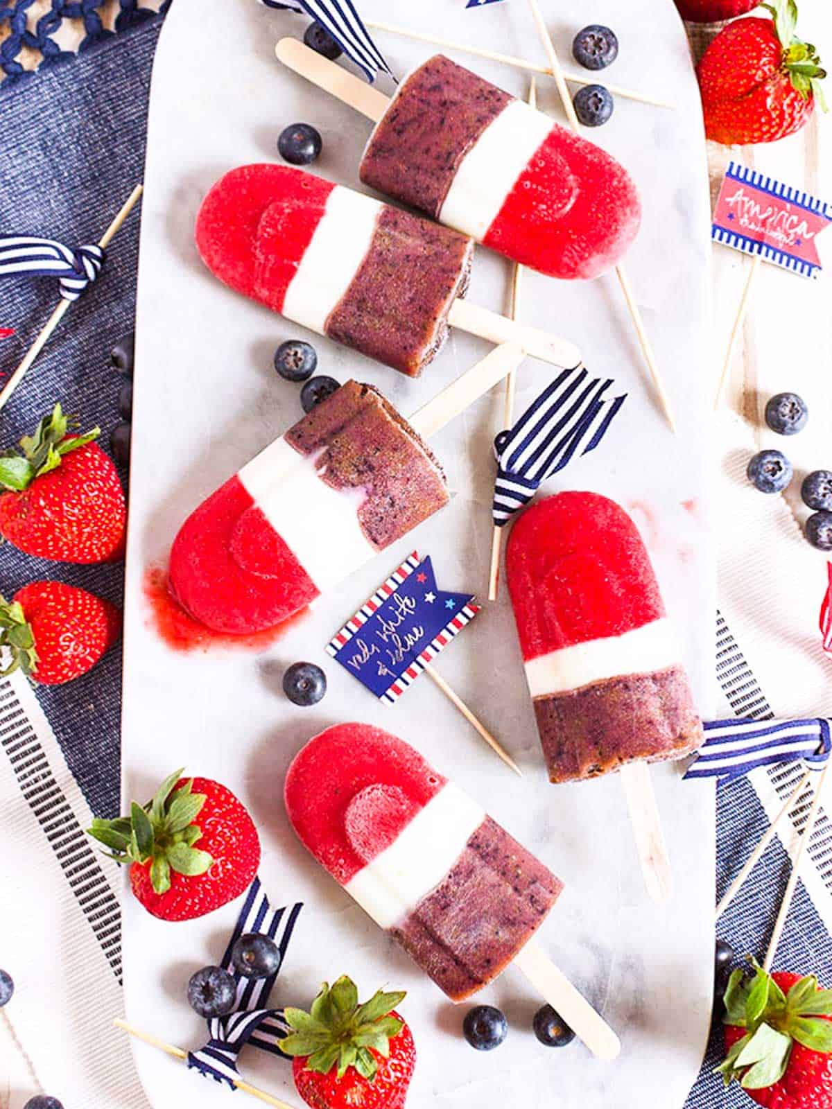Five red white blue smoothie popsicles on a tray with strawberries.
