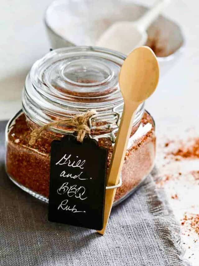 A glass jar filled with homemade grill and BBQ dry rub with a wooden spoon attached for a gift.