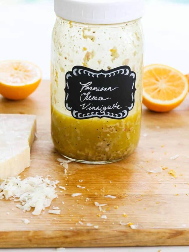 A large mason jar labeled Parmesan Lemon Vinaigrette with dressing inside on a cutting board.