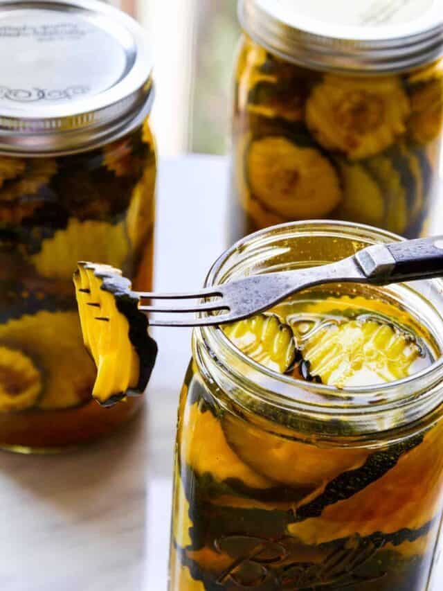 A wavy zucchini pickle on an antique fork resting on top of an open Mason jar.