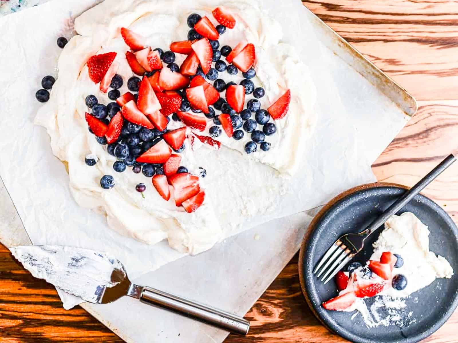 A white pavlova topped with blueberries and strawberries on a sheet pan.  