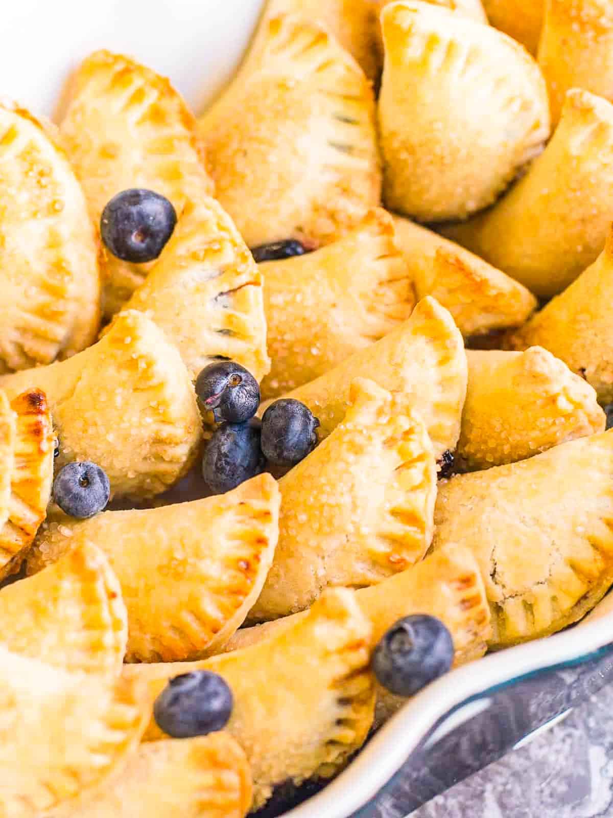 Mini blueberry hand pies in a dish all ready to eat garnished with blueberries. 