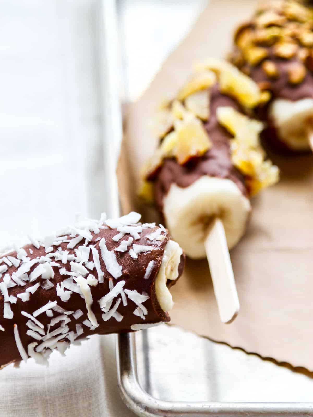 A frozen banana with a bite taken out of it resting on the edge of an aluminum sheet pan.