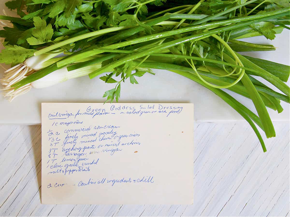 A bunch of green onions and a recipe card for green goddess salad dressing handwritten. 