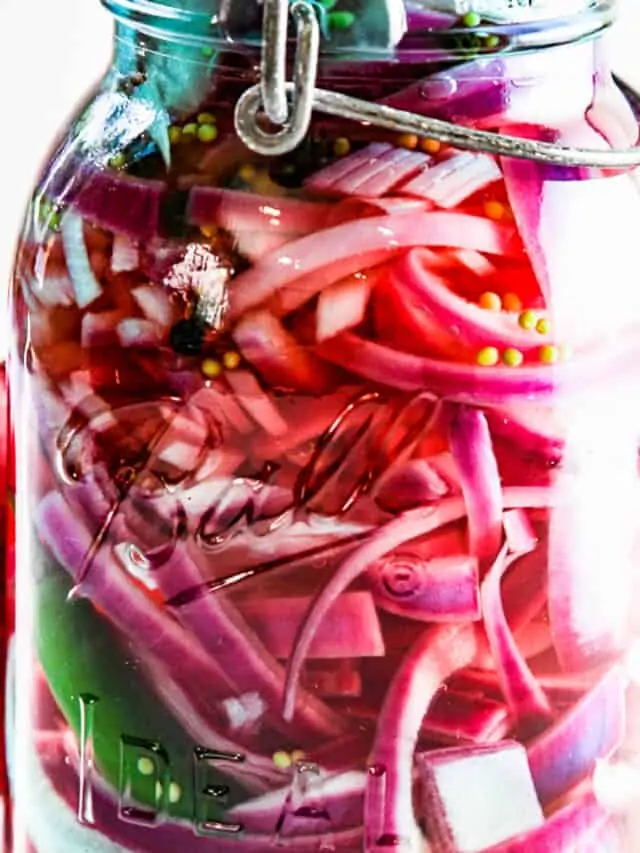 A tall aqua blue vintage glass clamp jar with red onions and green chile and garlic in the jar.