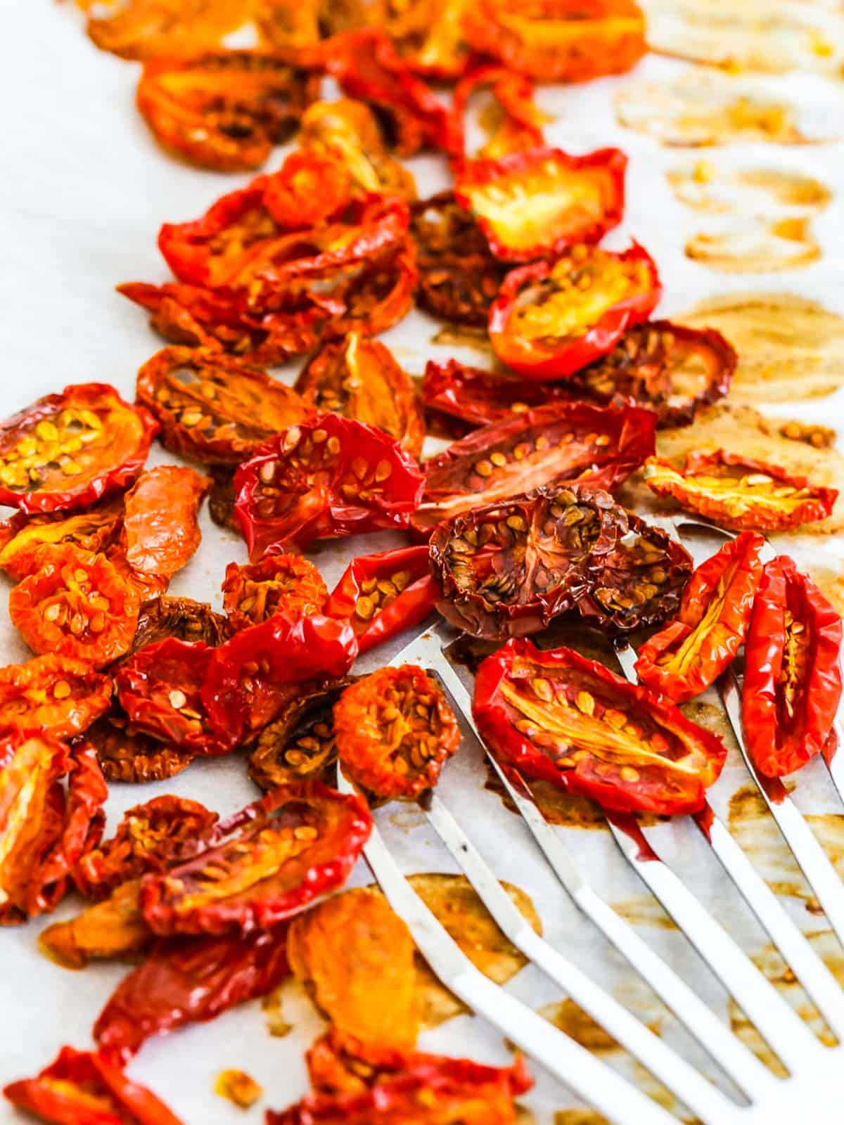 A wire spatula scooping up sun dried tomatoes that were oven baked on a sheet pan.