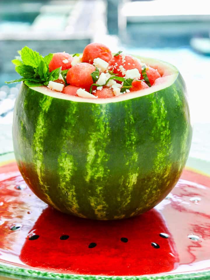 A watermelon carved out full of watermelon balls and topped with mint and feta cheese.