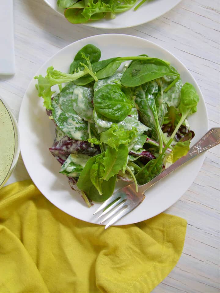 Small white plate with silver fork and greens tossed in green goddess salad dressing.