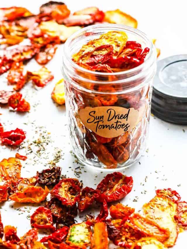 A clear glass canning jar filled with Sun Dried Tomatoes and a label on the front with them scattered dried tomatoes on the table.