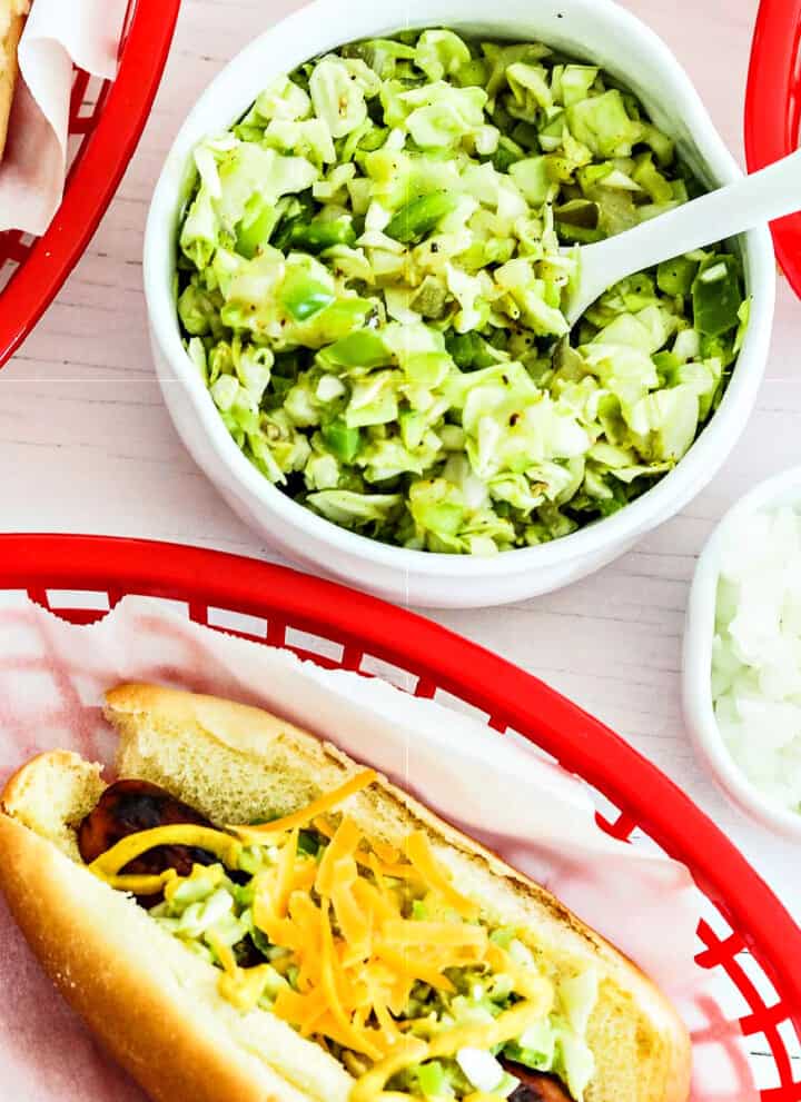 A small white bowl with homemade relish in to top hot dogs in paper lined baskets.