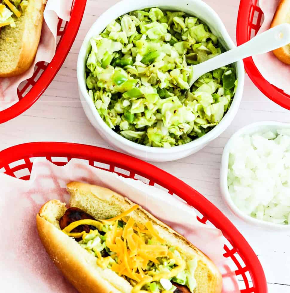 A small white bowl with homemade relish in to top hot dogs in paper lined baskets.