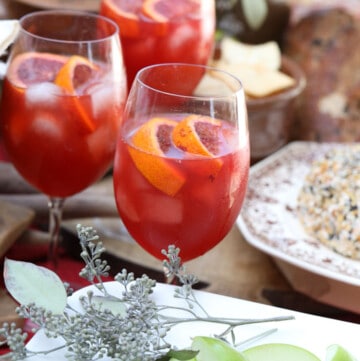 Three glasses of Aperol Spritz on a table with appetizers at a Fall party.
