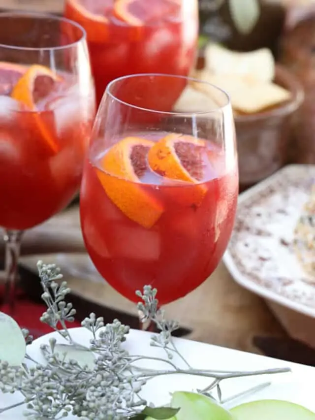 Three glasses of Aperol Spritz on a table with appetizers at a Fall party.
