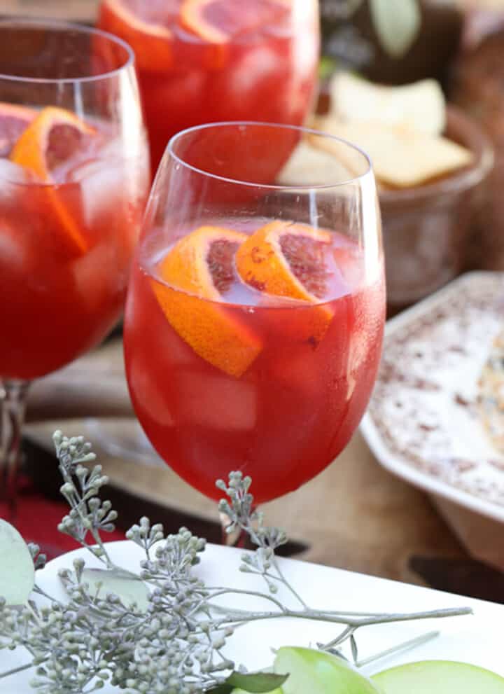 Three glasses of Aperol Spritz on a table with appetizers at a Fall party.