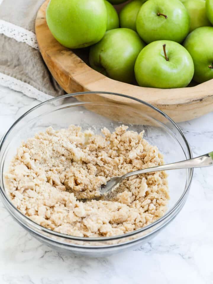 A clear glass bowl with crumble topping to put in a recipe for apple crumble pie or dutch apple pie.