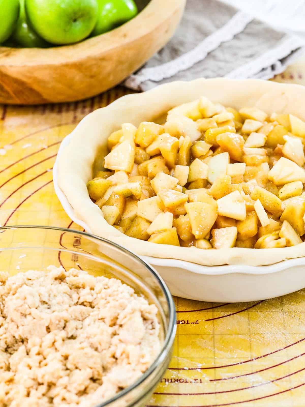 A white pie dish with pie dough filled with apple pie filling ready to bake.