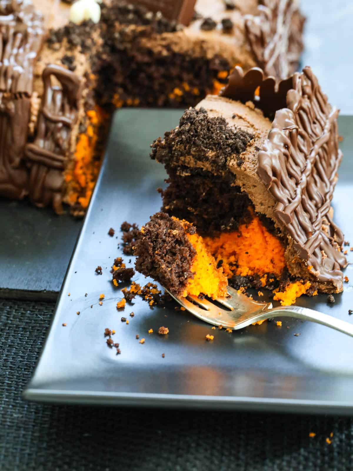 A slice of orange and chocolate Halloween cake on a black plate with a fork. 