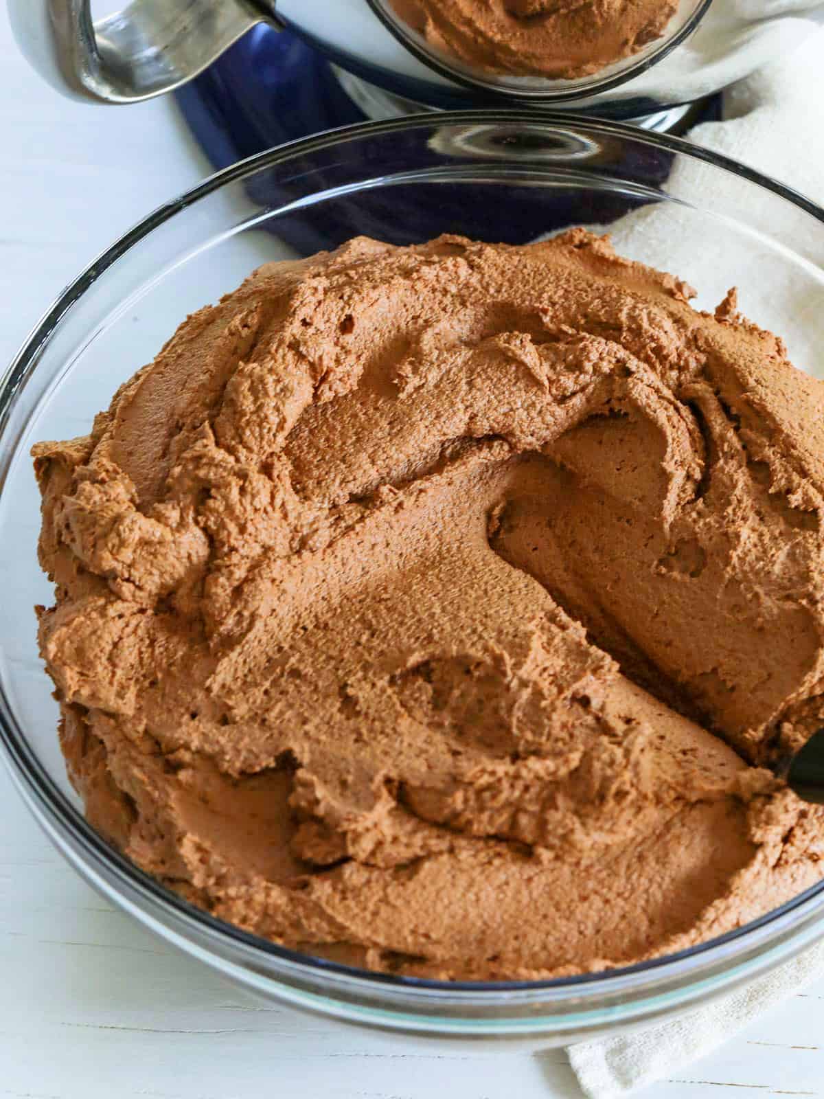 A large glass bowl full of chocolate frosting with a small offset spatula ready to frost a cupcake or cake.