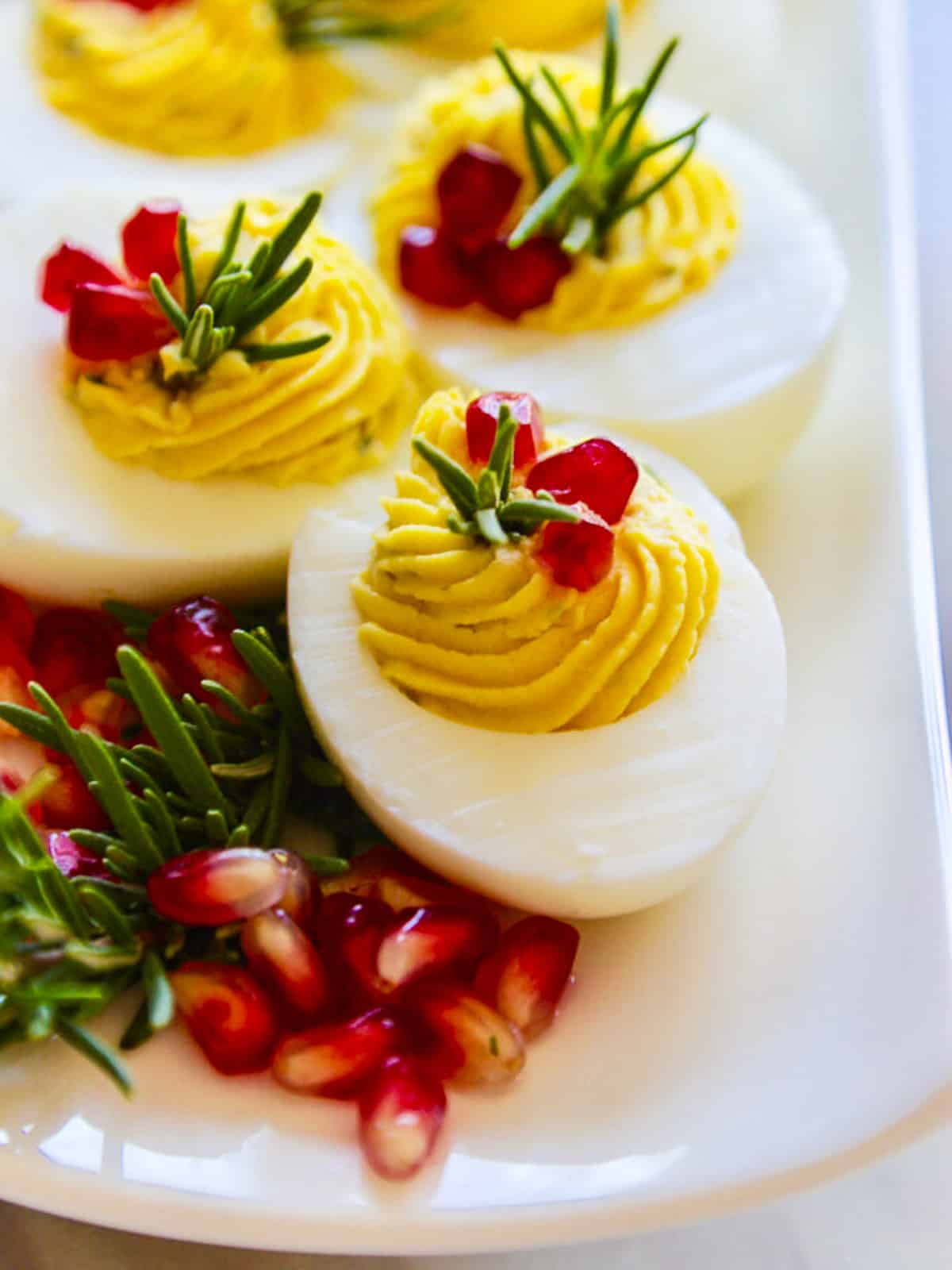 White long platter with gorgeous Christmas Deviled Eggs decorated with rosemary and pomegranate seeds.