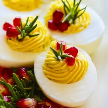 White platter with Christmas Deviled Eggs garnished with rosemary and pomegranate seeds.