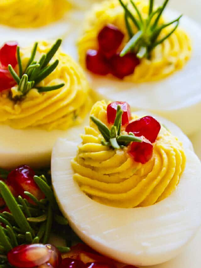 White platter with Christmas Deviled Eggs garnished with rosemary and pomegranate seeds.