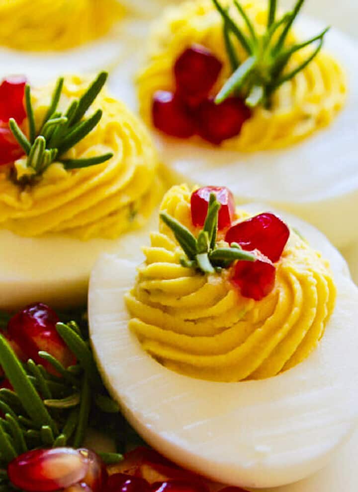 White platter with Christmas Deviled Eggs garnished with rosemary and pomegranate seeds.