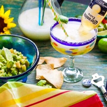 A Mexican glass with a slushy margarita, garnished with a lime and coronita bottle.