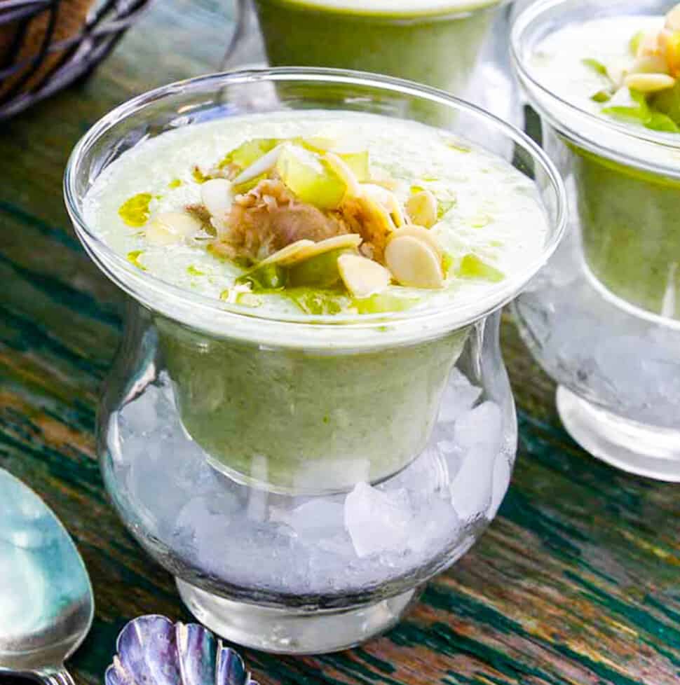 Chilled cucumber soup topped with crab meat and grape garnish served in bowls over ice.