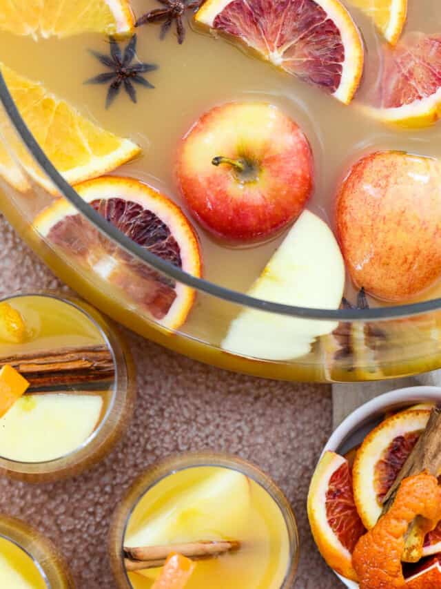 A large glass punch bowl filled with Fall and Thanksgiving punch with apples and oranges floating on top.