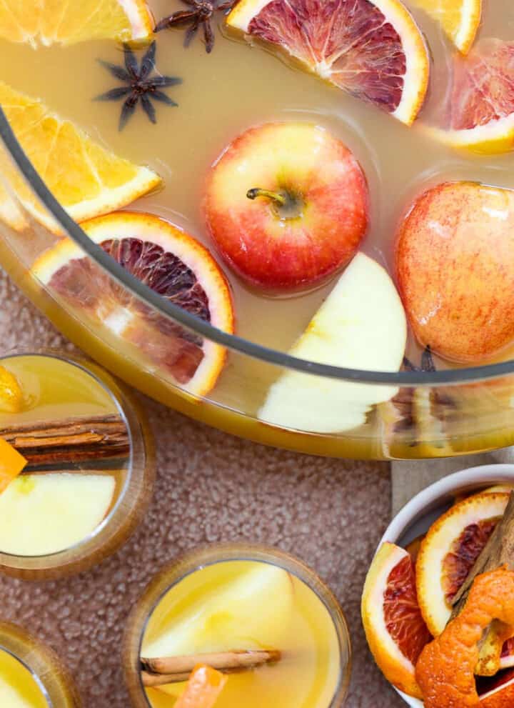 A large glass punch bowl filled with Fall and Thanksgiving punch with apples and oranges floating on top.