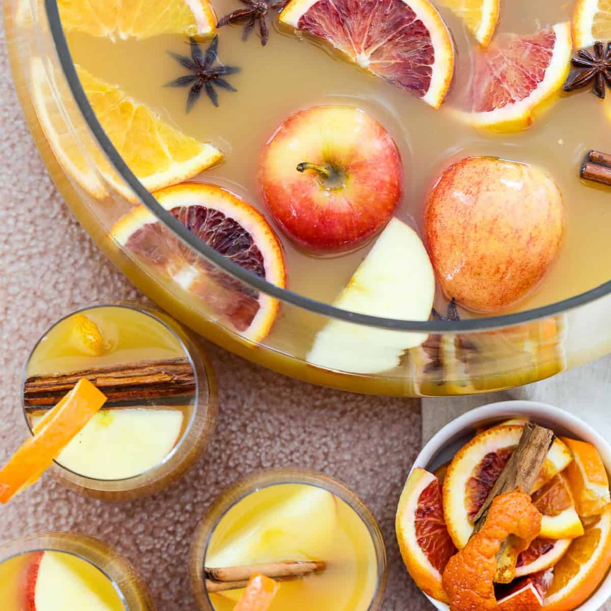 A large glass punch bowl filled with Fall and Thanksgiving punch with apples and oranges floating on top.