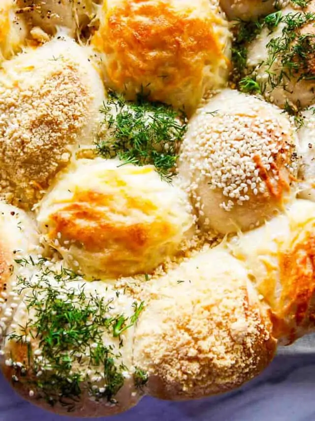 A close up of baked Frozen Dinner Rolls topped with cheeses, herbs, and seasonings.