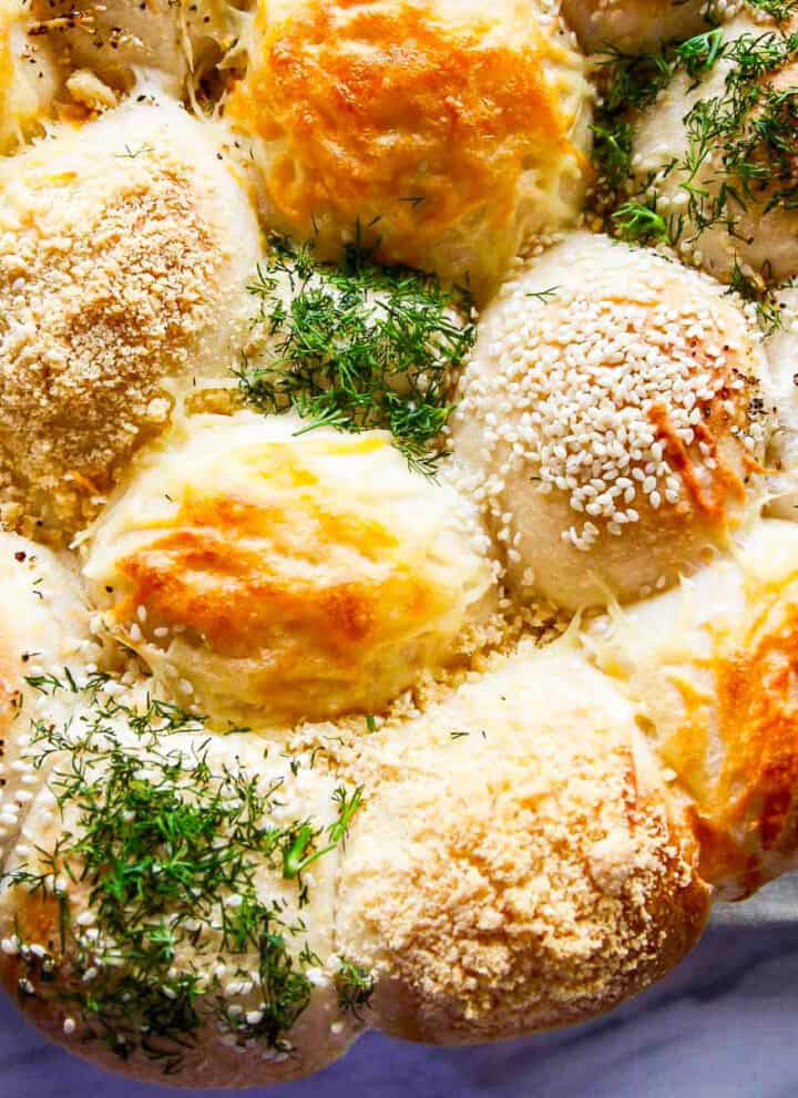 A close up of baked Frozen Dinner Rolls topped with cheeses, herbs, and seasonings.