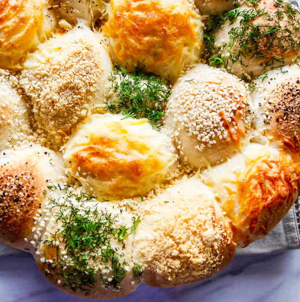 A close up of baked Frozen Dinner Rolls topped with cheeses, herbs, and seasonings.