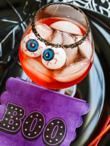 A large cocktail glass with black sugar rim, ice, Aperol Cocktails, and eyeballs for Halloween.