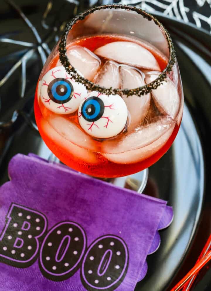 A large cocktail glass with black sugar rim, ice, Aperol Cocktails, and eyeballs for Halloween.