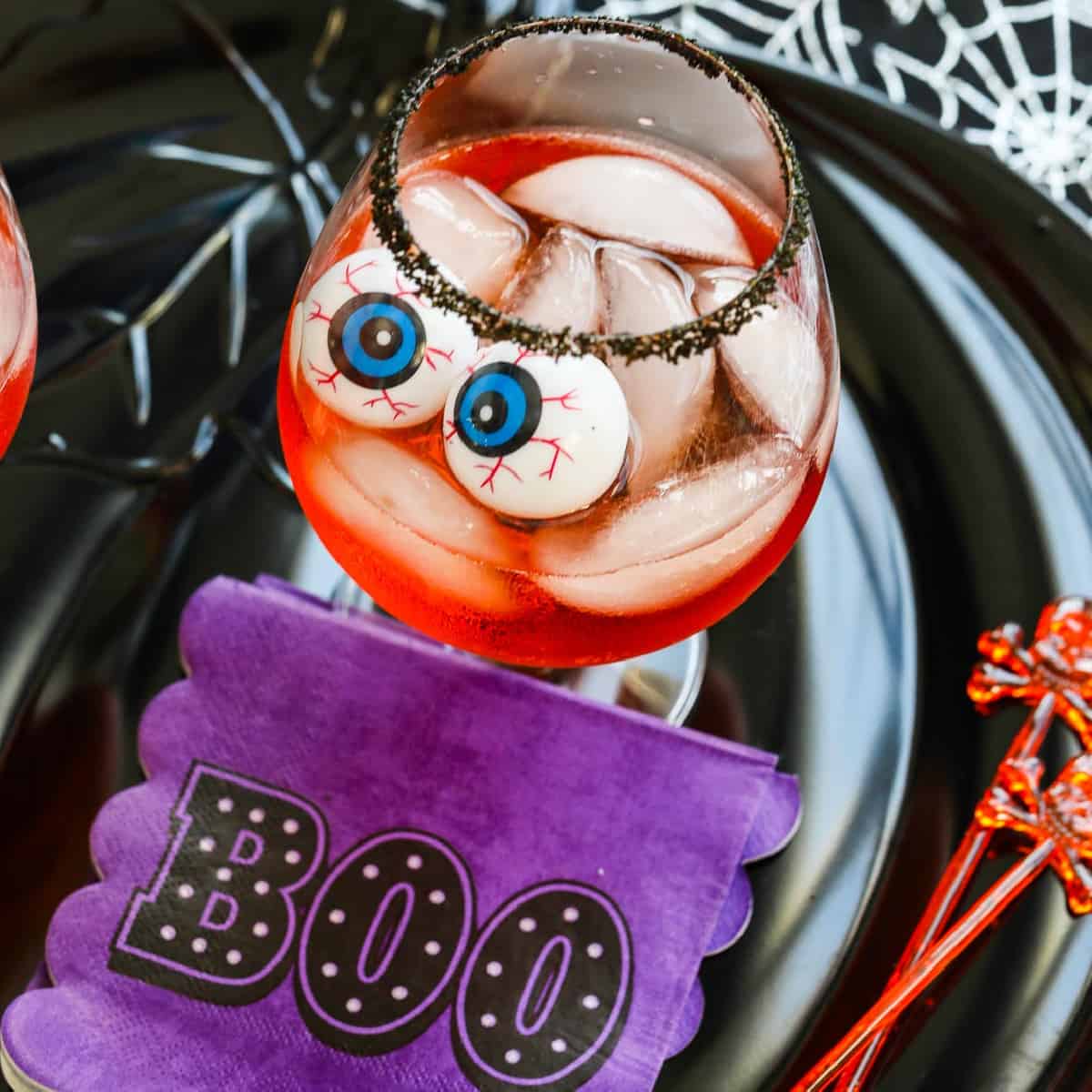 A large cocktail glass with black sugar rim, ice, Aperol Cocktails, and eyeballs for Halloween.