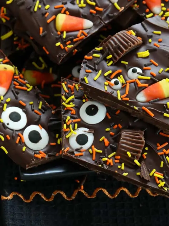 A pile of Halloween bark on a dark black platter decorated with candy and sprinkles.