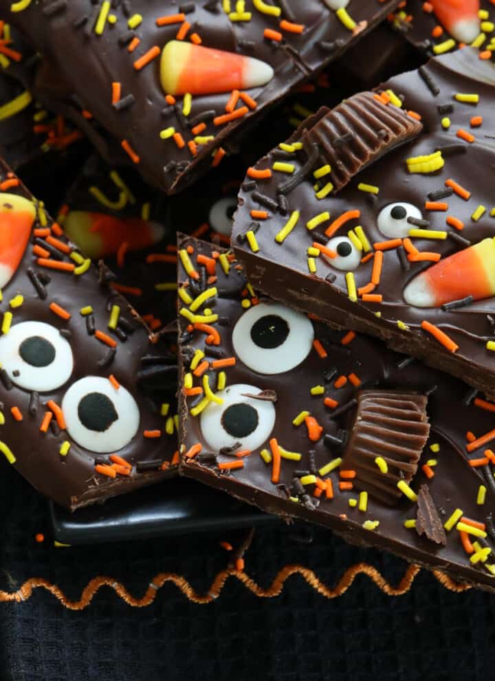 A pile of Halloween bark on a dark black platter decorated with candy and sprinkles.