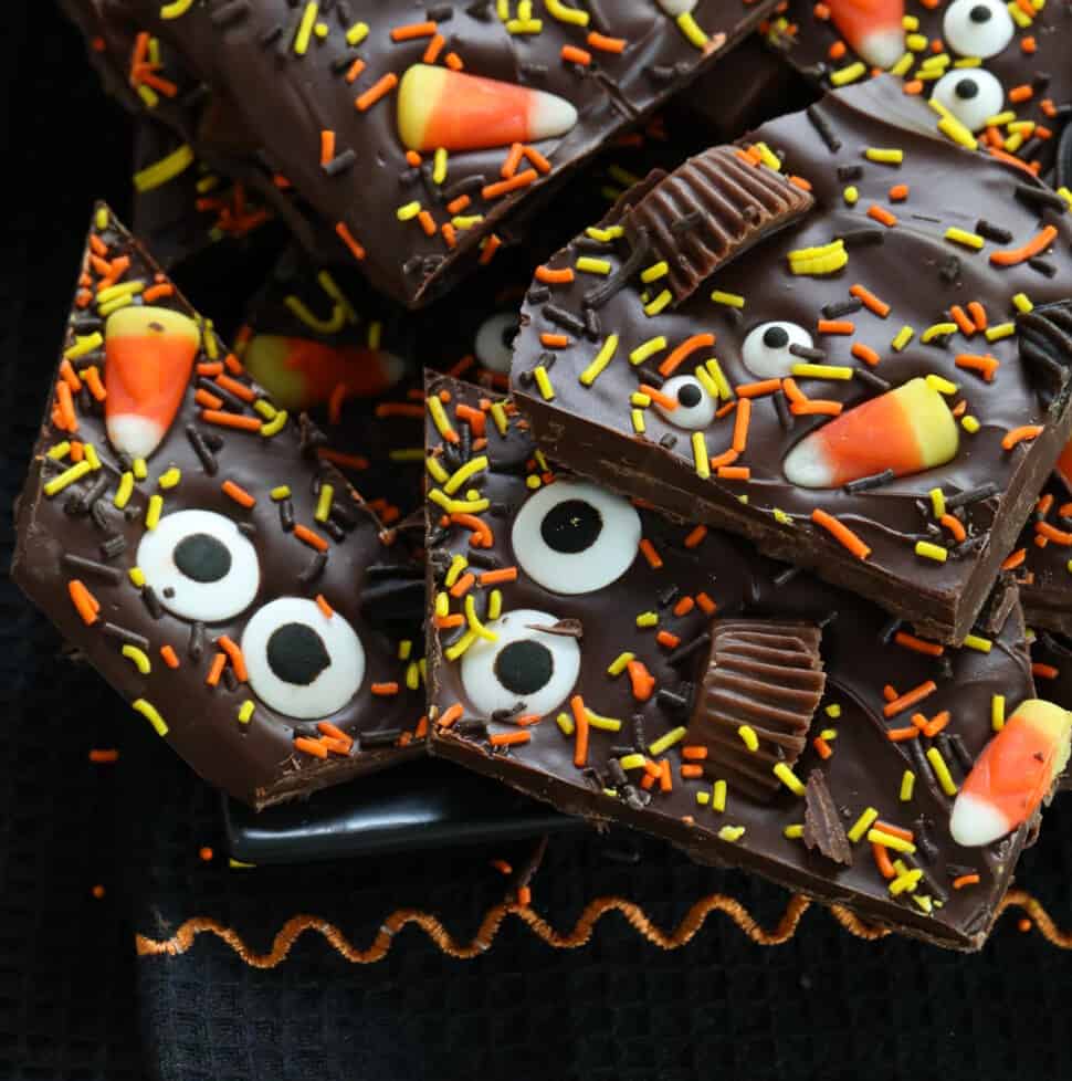 A pile of Halloween bark on a dark black platter decorated with candy and sprinkles.