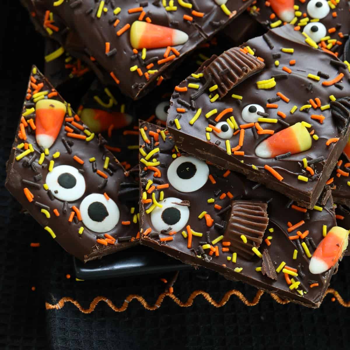 A pile of Halloween bark on a dark black platter decorated with candy and sprinkles.