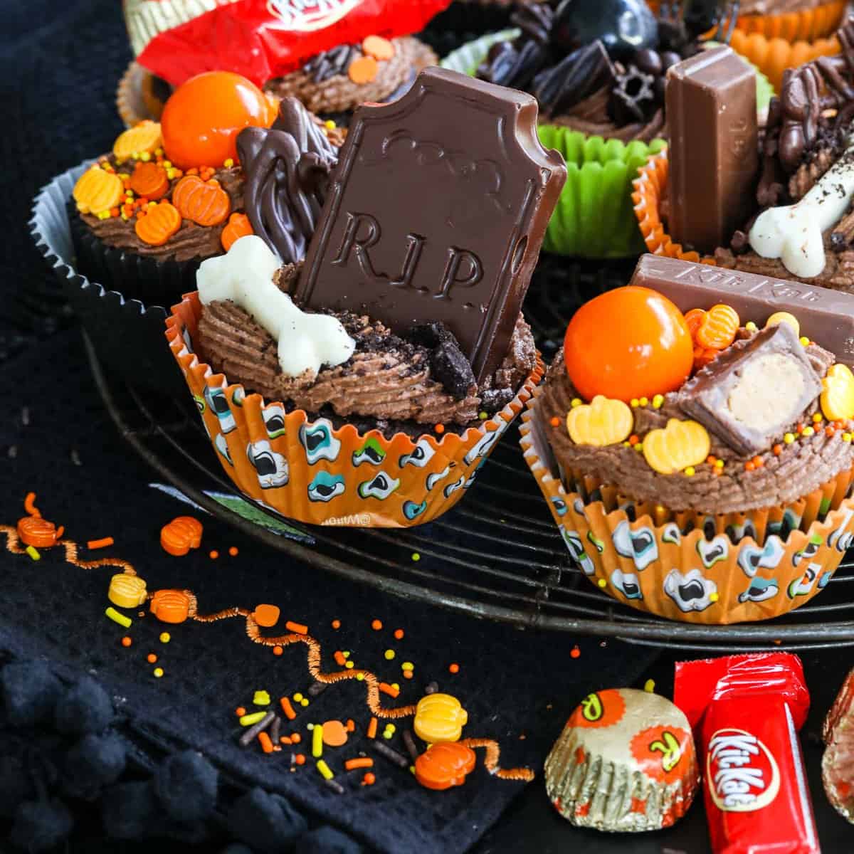 Close up of decorated Halloween cupcake ideas with chocolate frosting, candy, sprinkles on a vintage cooling rack.